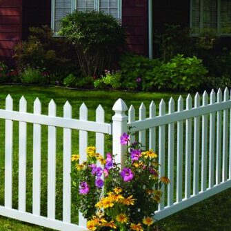 Classic white picket fence installed in a well-manicured garden with colorful flowers.