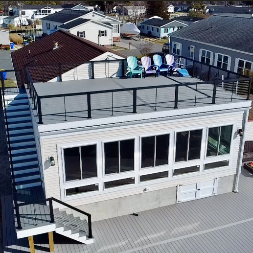 Modern waterfront home featuring a spacious Trex deck with rooftop seating and glass windows overlooking the water.