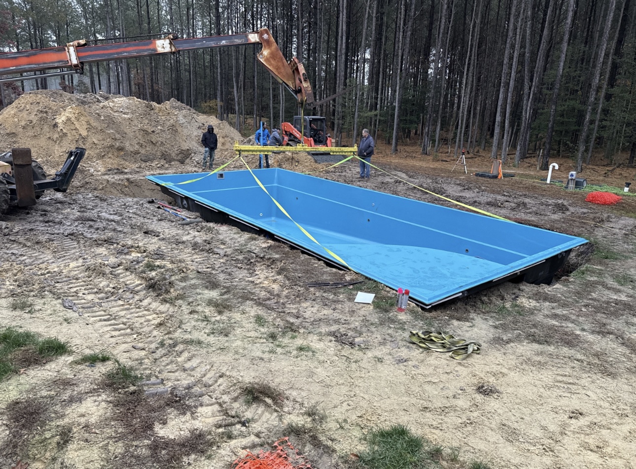 A large blue fiberglass Leisure Pool being lowered by a crane into a prepared backyard excavation site.