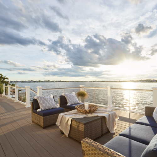 Luxury custom deck with wicker outdoor furniture overlooking a calm bay at sunset.