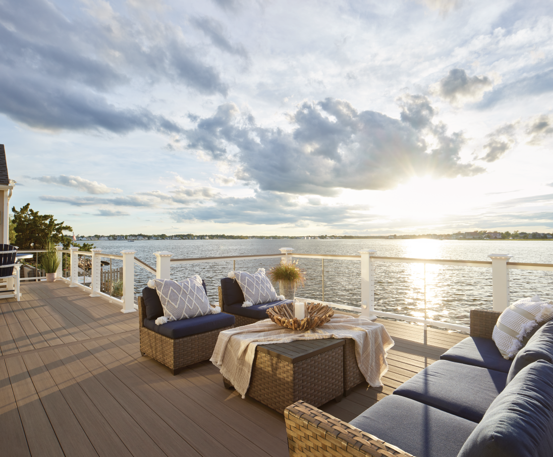 Luxury custom deck with wicker outdoor furniture overlooking a calm bay at sunset.