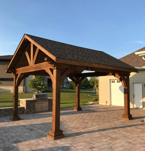 A heavy-timber custom cedar pavilion with a gabled roof and decorative braces installed on a backyard patio in Delaware.