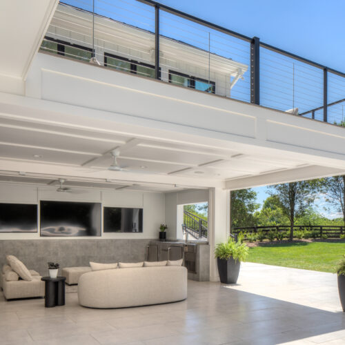 Modern white covered patio featuring Trex Signature X-Series black cable railing, comfortable outdoor sectional seating, and a mounted TV.