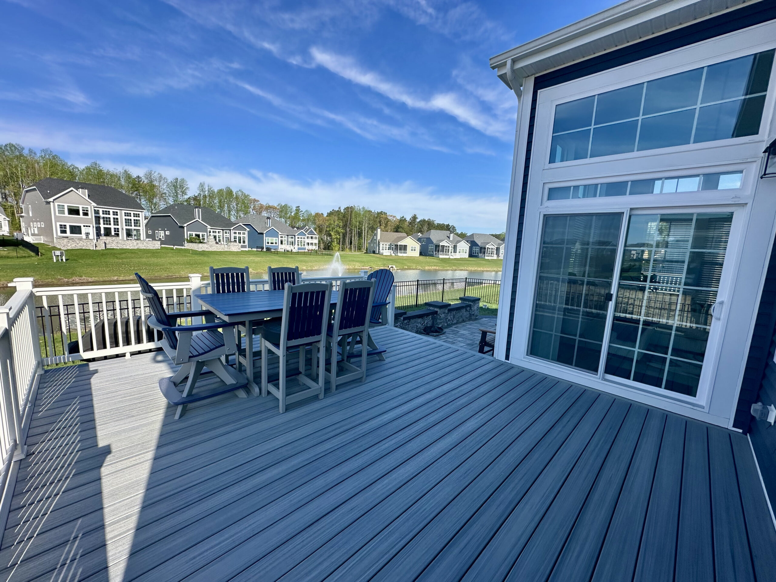 A grey composite deck with white railings and stairs leading down to a custom stone paver patio in a backyard.
