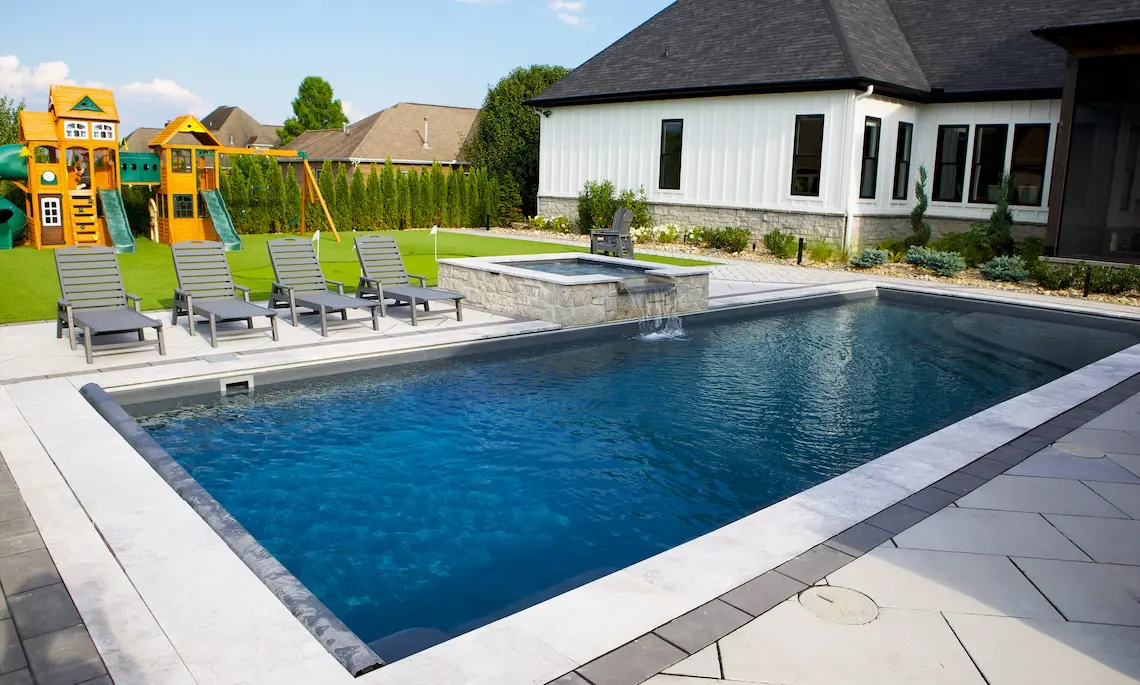 The Wave model fiberglass pool featuring a curvy freeform design, a built-in splash pad, and full-length bench seating.
